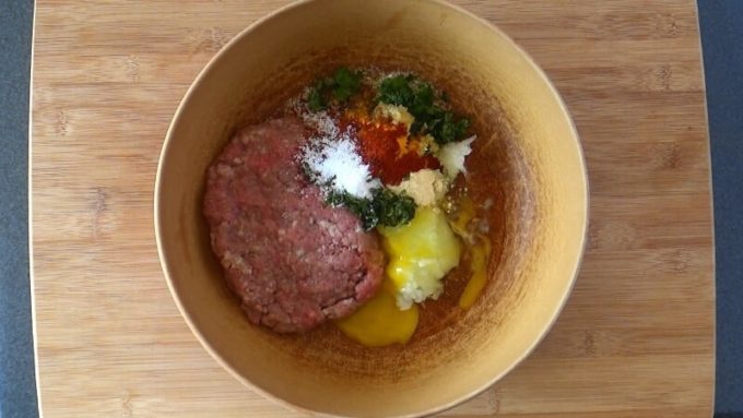 Ground meat with grated onions, egg, bread crumbs, herbs and spices in a mixing bowl for making meatballs.