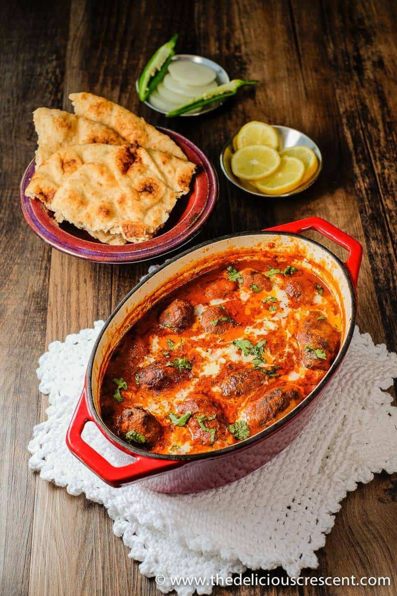 Kofta curry is a delicious dish of succulent grilled or broiled beef meatballs in a rich, creamy and spicy sauce. It is full of fragrant Indian spices and makes a great weeknight dinner. This easy low carb meatball curry recipe is also freezer friendly. Great tips for lightening up the sauce included. Make it with ground lamb or gluten free. #Indianfood #kofta #curry #beef Kofta curry served in a cast iron dish with some naan and lemon slices.