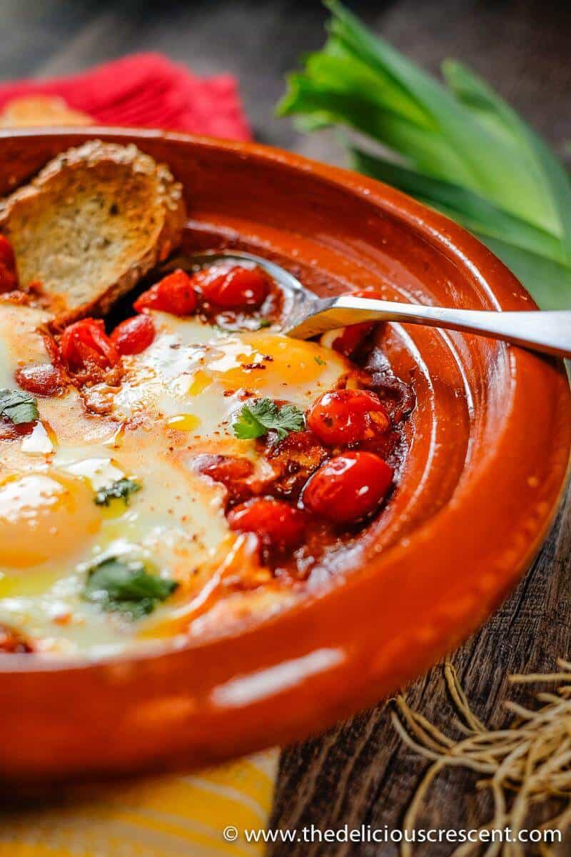 Moroccan Eggs in Tomato Sauce with a piece of bread and a spoon.