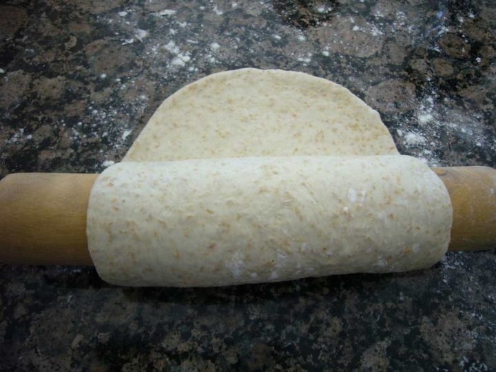 Flat bread being lifted with the help of a rolling pin.