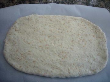 Flat bread rolled out and placed on parchment paper.