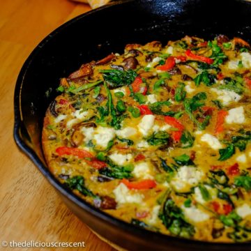 Mushroom frittata with spinach, red pepper and cheese baked in a cast iron skillet.