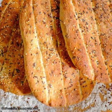 Several Persian barbari bread loaves placed on a table with flour dusted around.