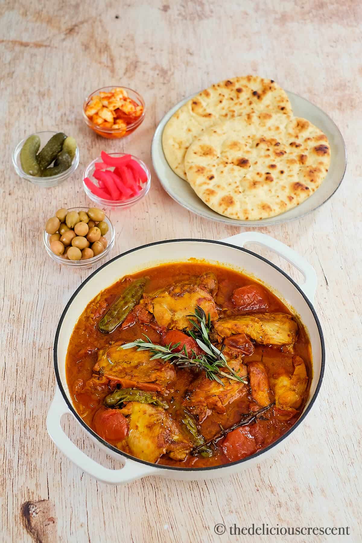 Tomato chicken cooked with rosemary and served on the table with bread.