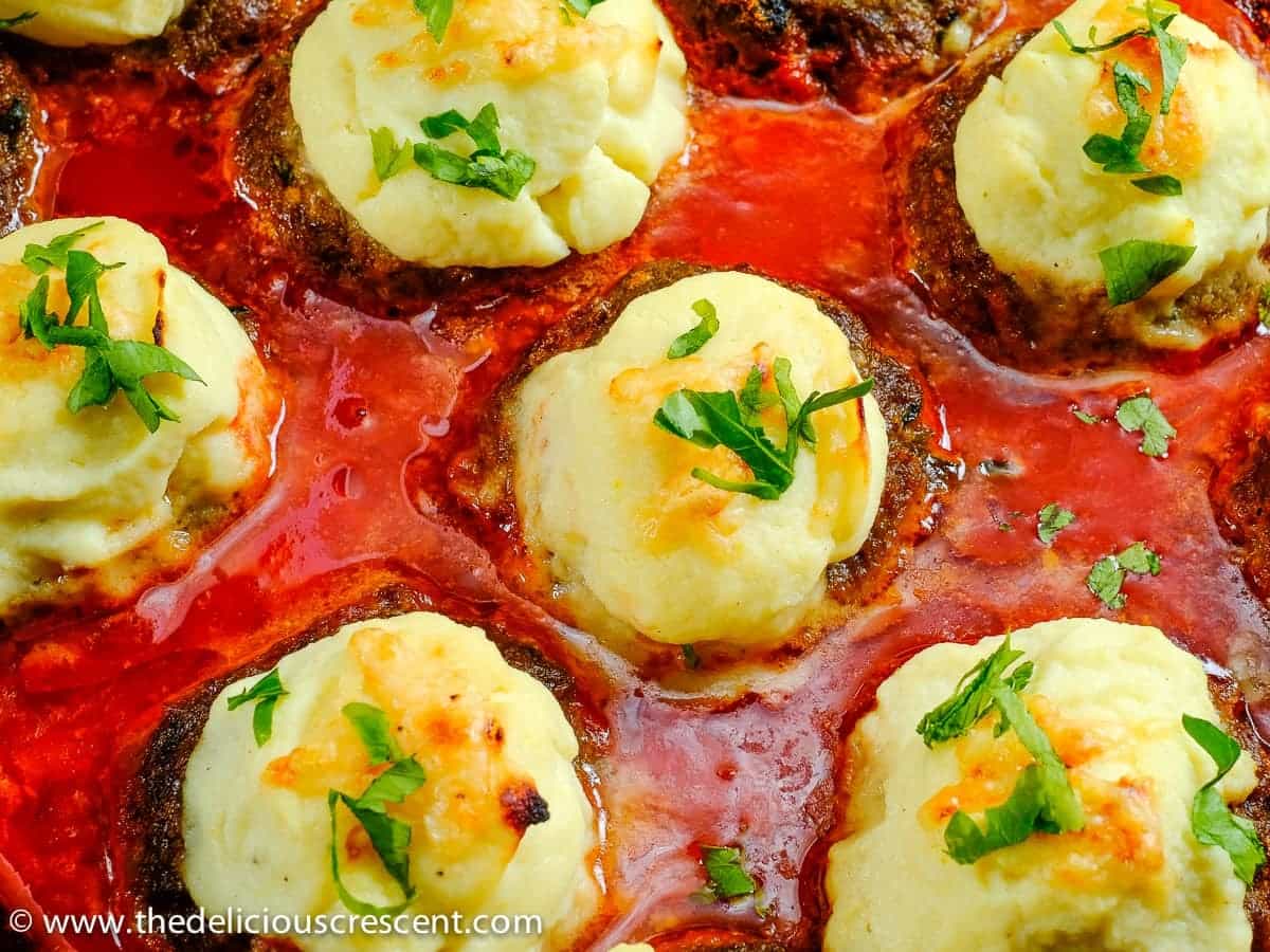 Creamy cauliflower stuffed meatballs is a tasty and healthy Mediterranean style kofta recipe made with ground beef, spices, herbs and stuffed with creamed cauliflower. The succulent koftas are baked in a rich tomato gravy loaded with flavor and great for a weeknight dinner. It could be a meal by itself or serve flat bread and salad on the side. Lighter and low carb when compared to its traditional inspiration. #meatballs #weeknightmeal #cauliflowerrecipe Close up view of Creamy Cauliflower Stuffed Meatballs (Pasha's Kofta)