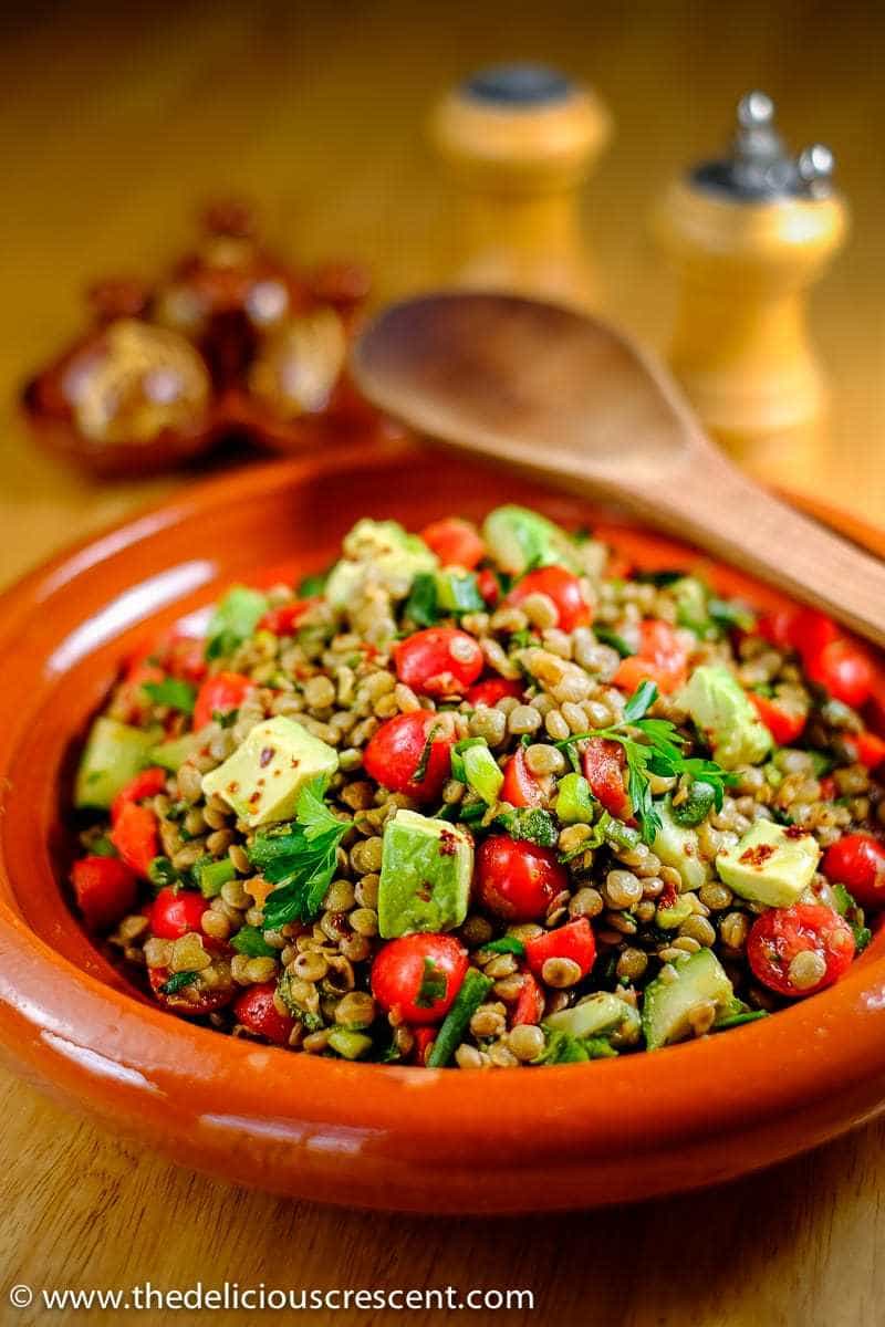 Spiced lentil salad with avocado served in a brown serving dish.