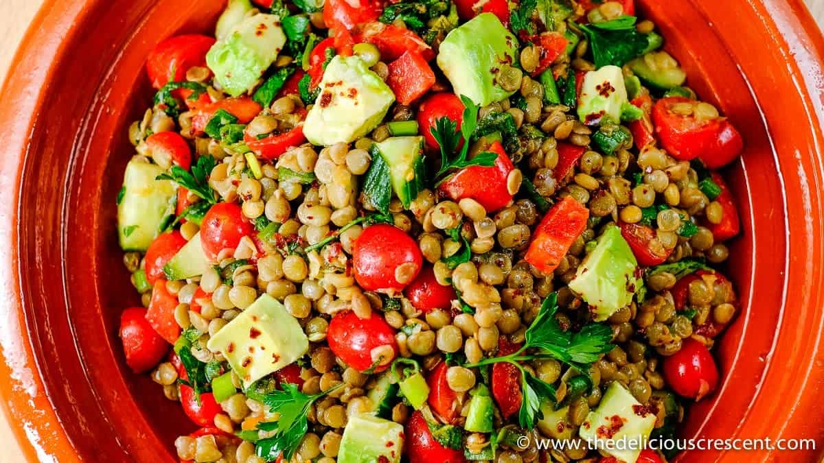 Close up view of spiced lentil salad with avocado served in a brown serving dish.
