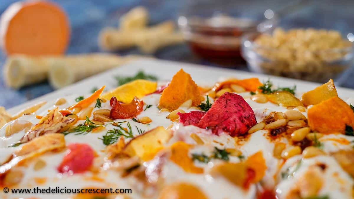 Close up view of chickpea salad with yogurt and vegetable chips served on a white plate placed on a blue table.