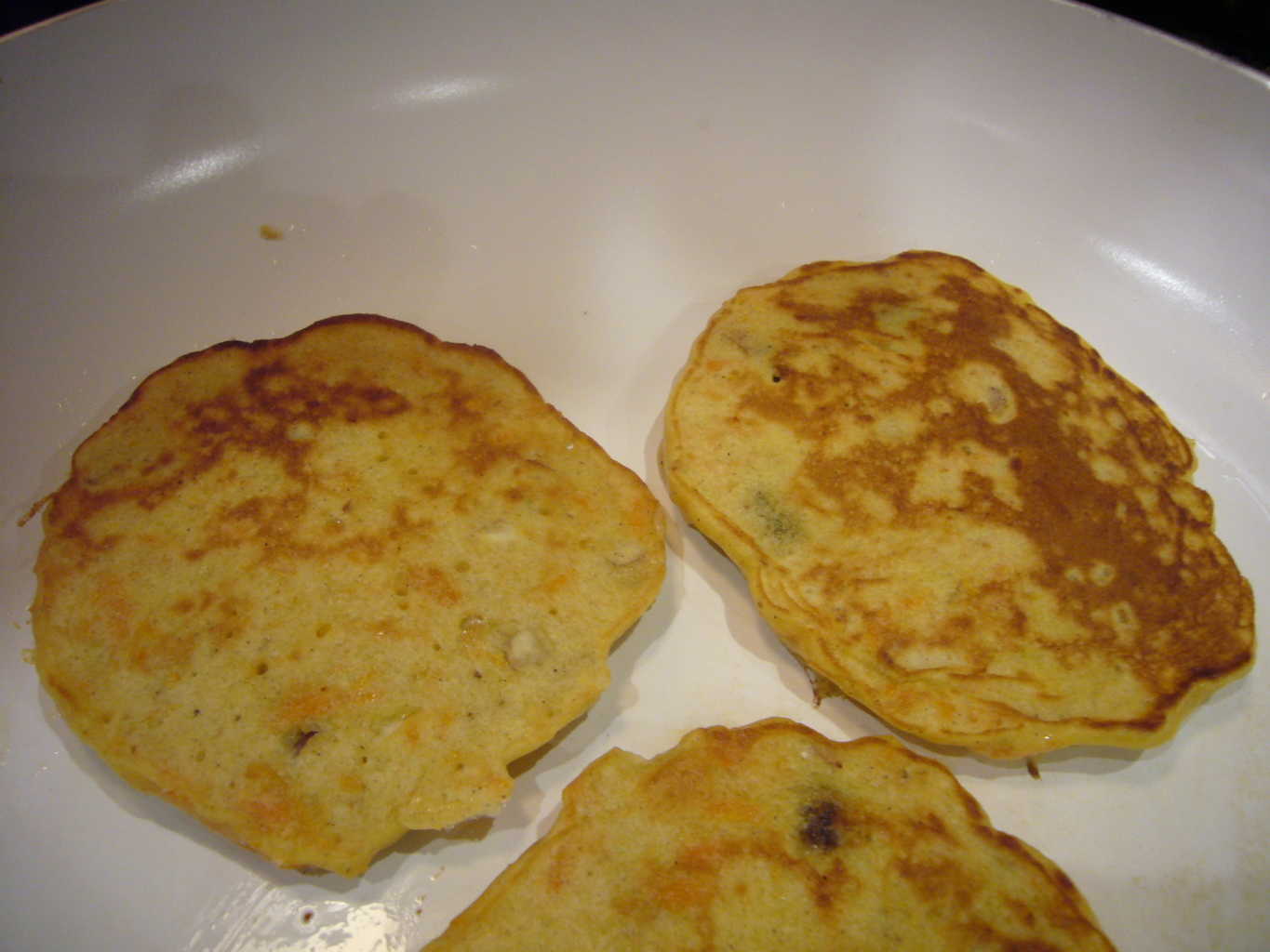 Three carrot pancakes flipped after cooking one side.