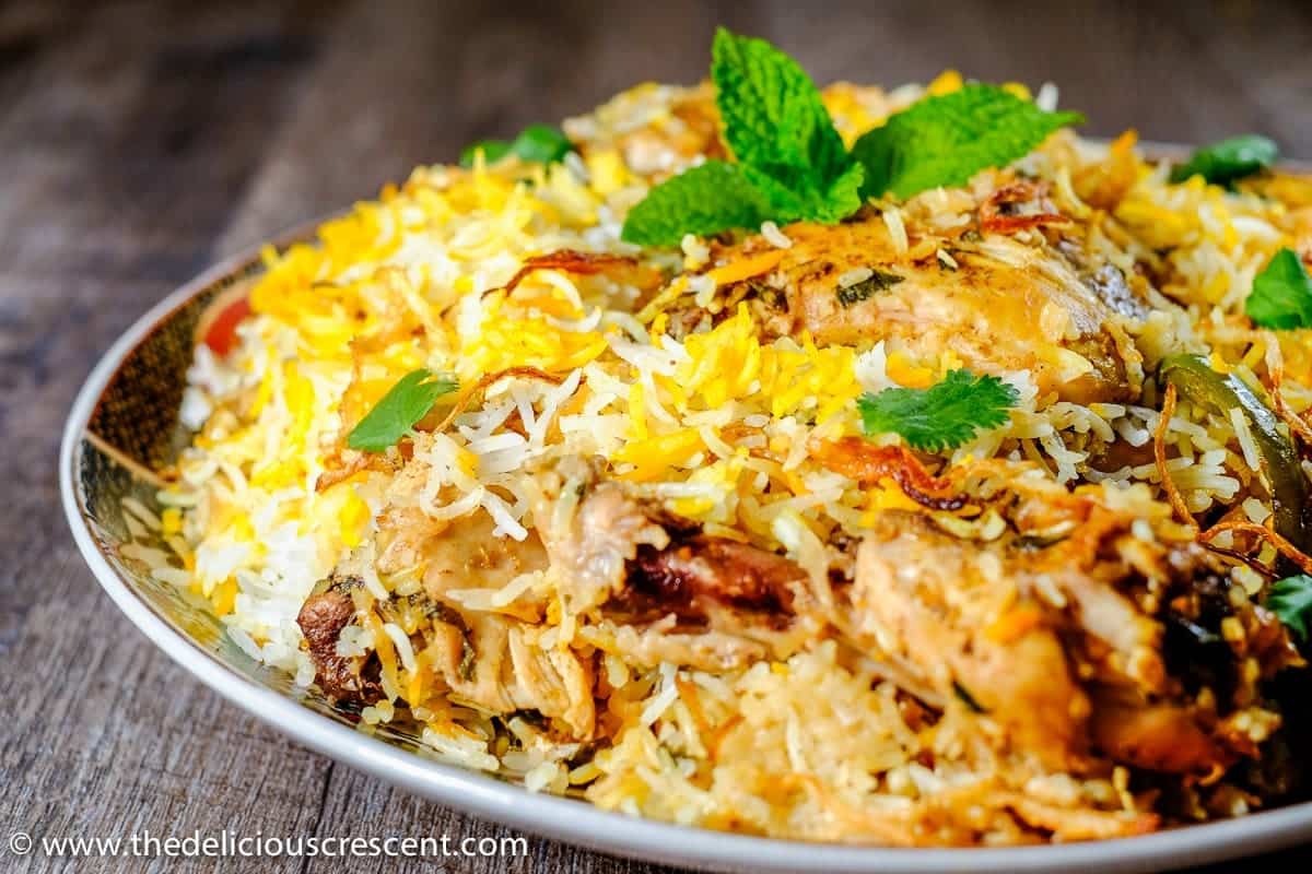 Front view of chicken biryani served in a round plate and topped with herbs.