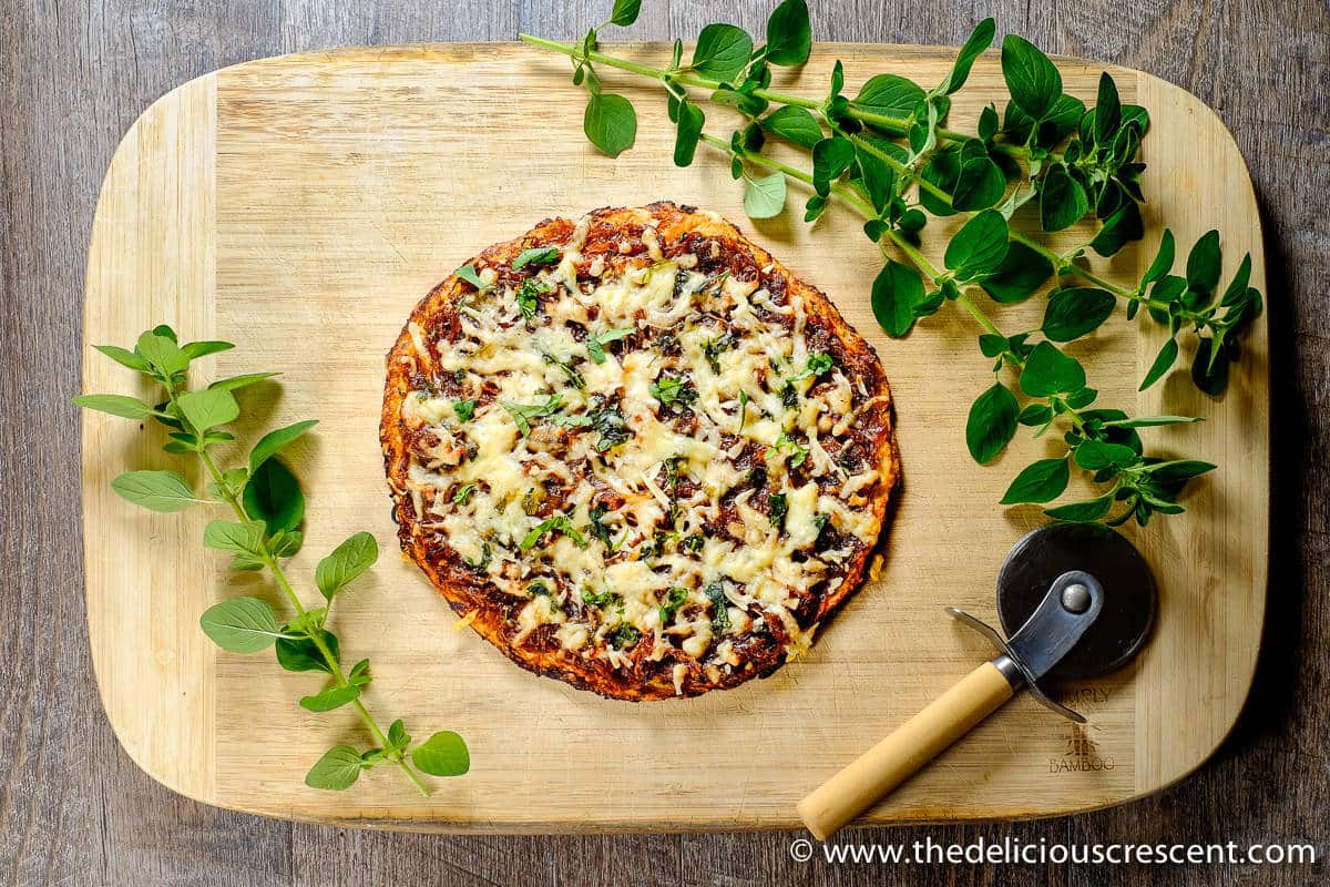 Cauliflower pizza on a wooden cutting board.