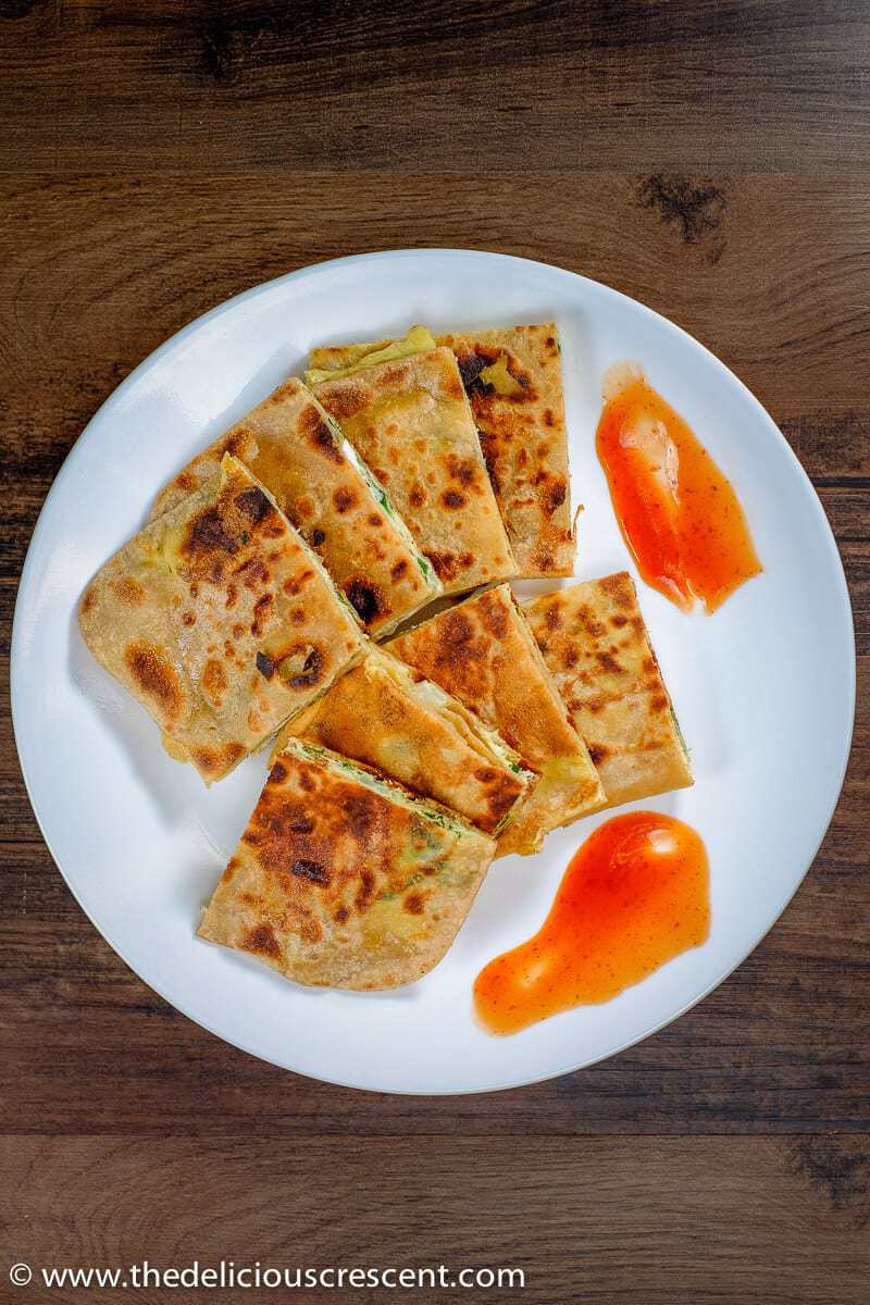 Overhead view of egg paratha served on a white plate with tomato sauce.