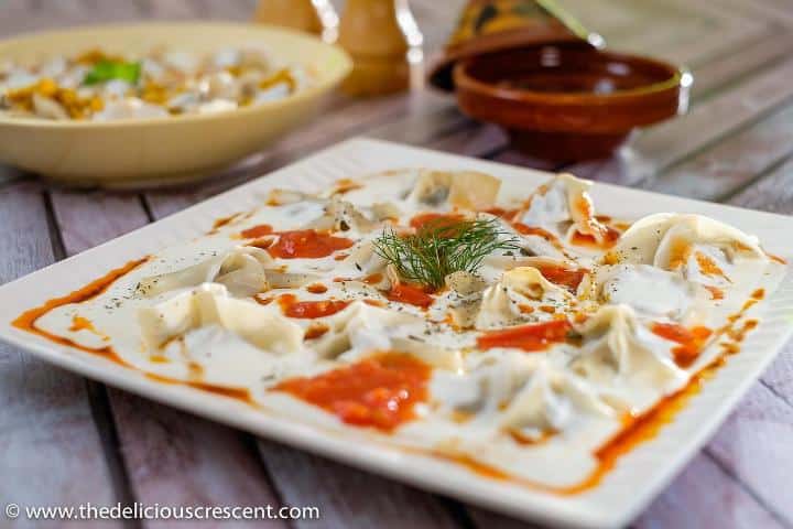 Manti dumplings served with a garlic yogurt sauce on a white plate.