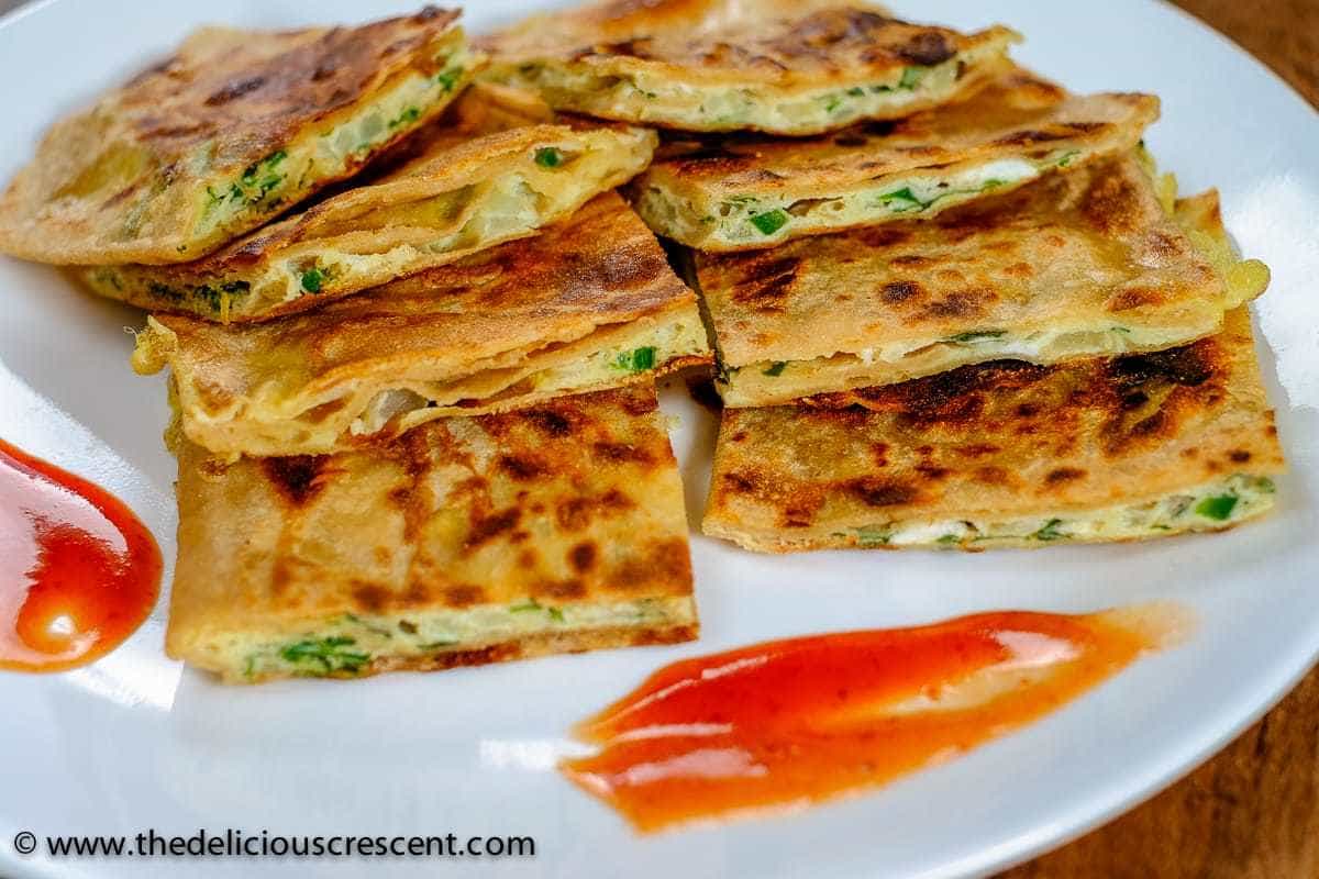 Egg paratha stuffed with omelette mixture, and cut into smaller pieces and served on a white plate.