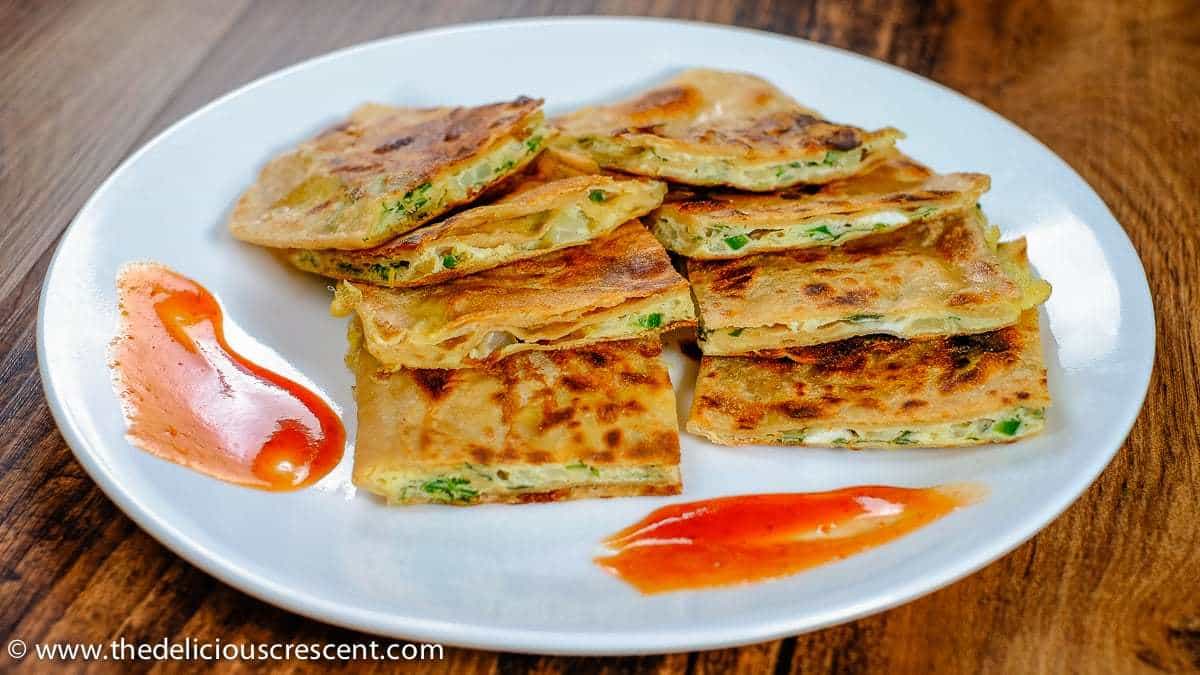 Front view of pieces of egg paratha served on a white plate.