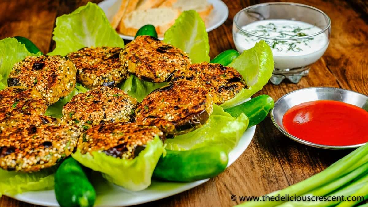 Eggplant patties arranged on lettuce in a white plate and served with dips.