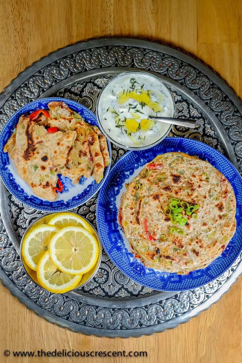 A stack of Indian flatbreads served in a blue plate with some yogurt in a bowl.