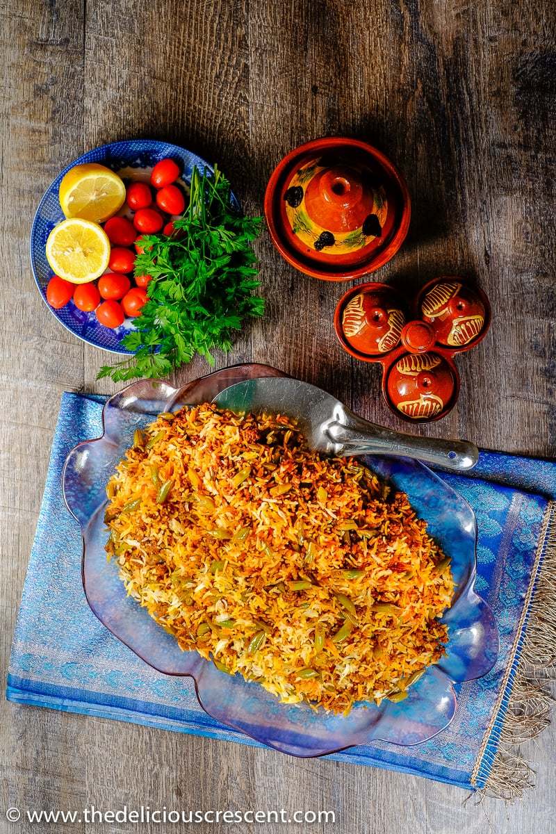 Overhead view of lubia polo served with fresh herbs, vegetables and pickles.