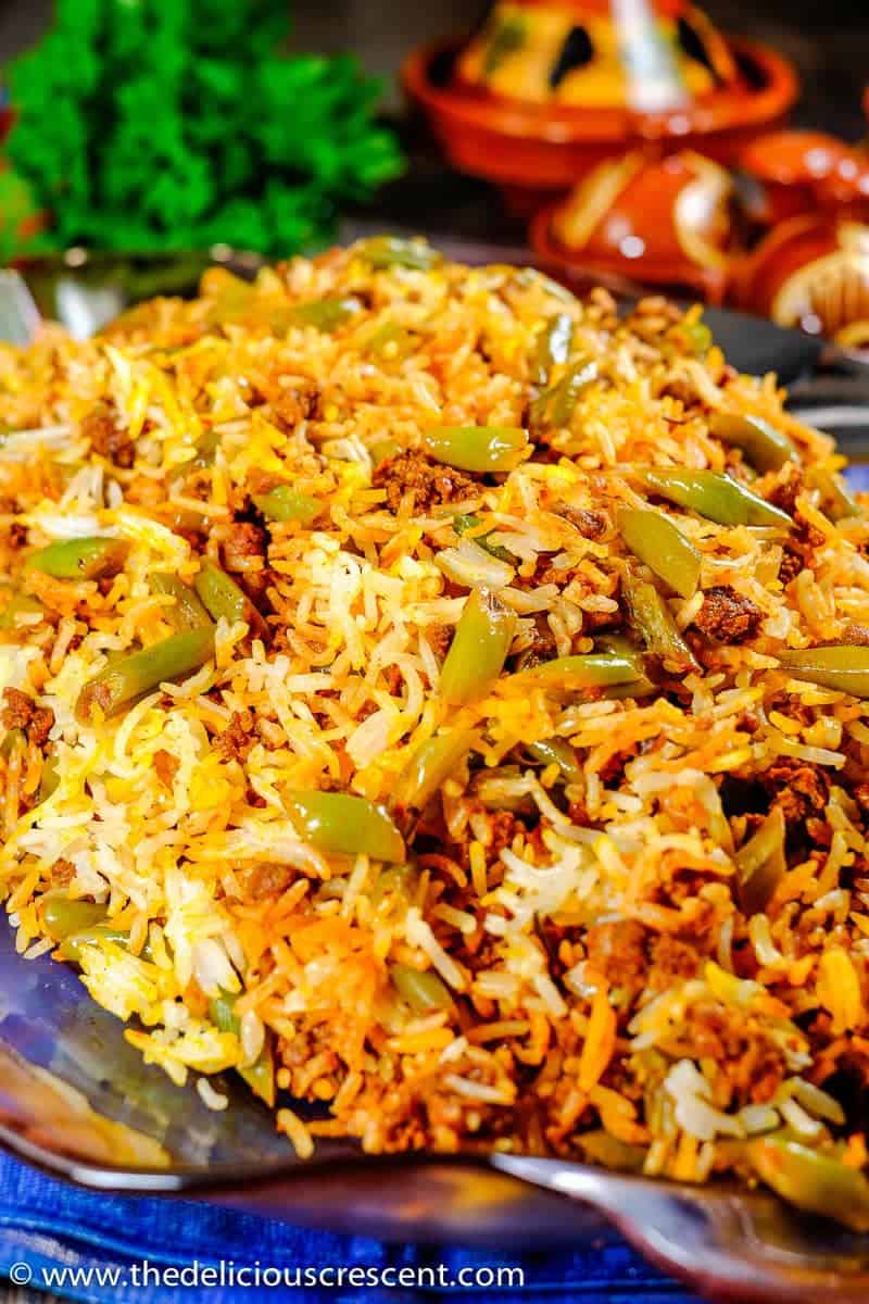 A big mound of Persian lubia polo served on a glass plate and placed on a table.