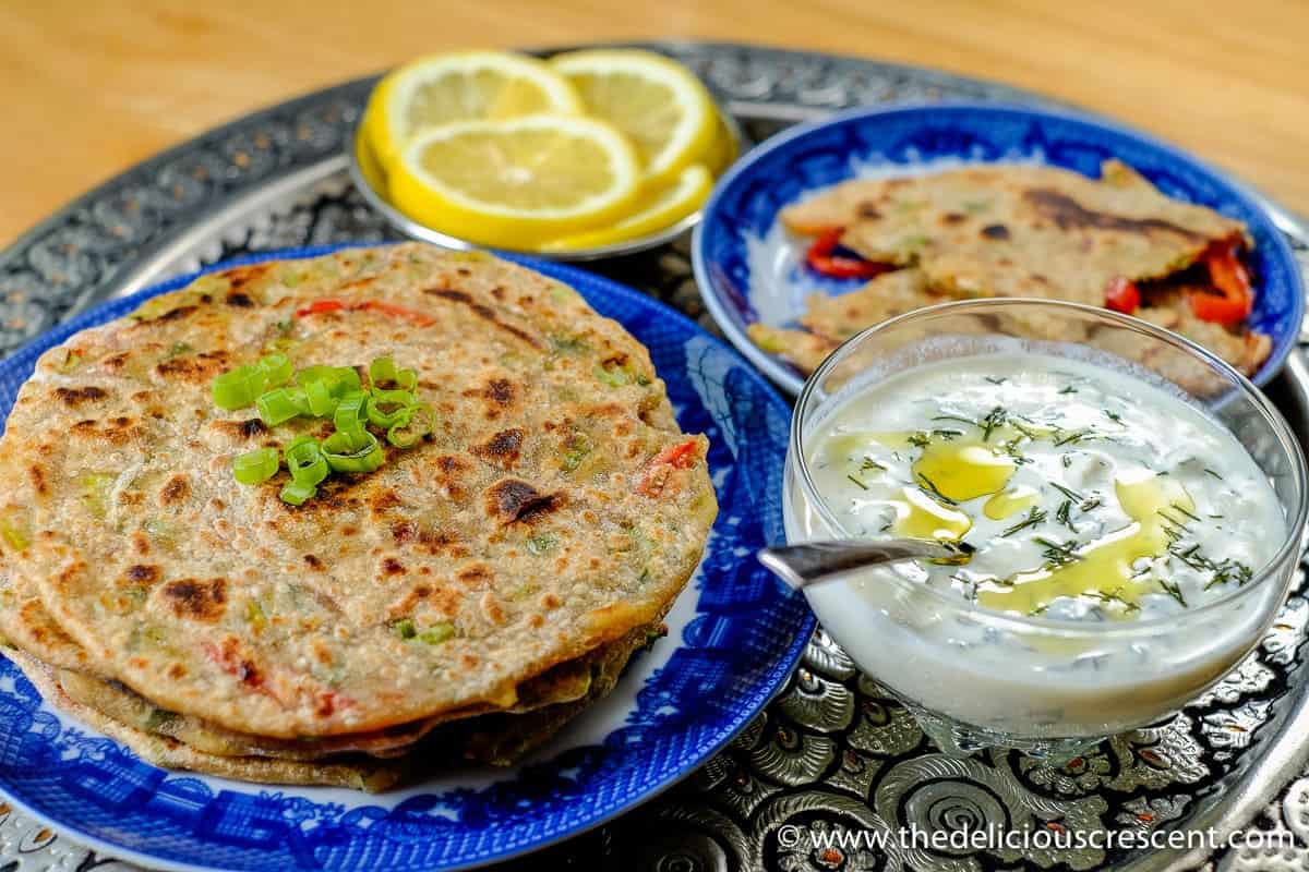 Indian stuffed flatbreads on a blue plate and served with yogurt.