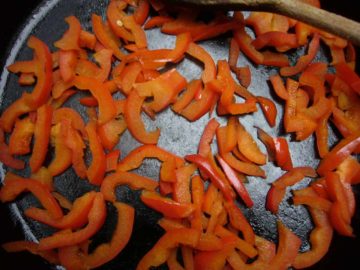 Red bell pepper sliced sauteed in a skillet.