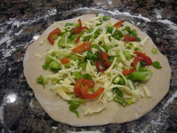 Paratha dough topped with cheese and chopped scallions, red bell peppers.