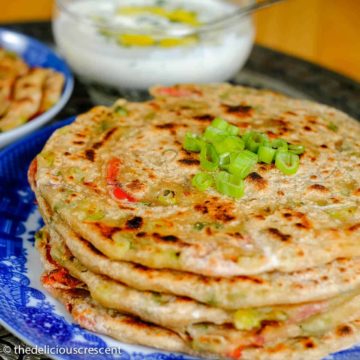 Cheese stuffed spring onion parathas stacked on a plate.