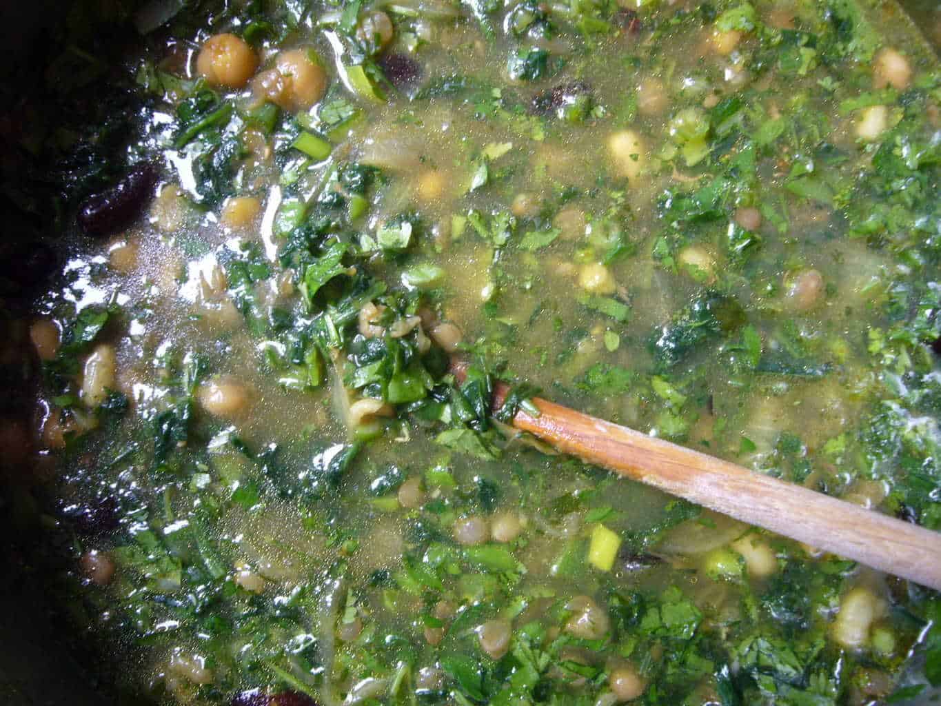 Beans, greens, herbs and spices being cooked to make noodle soup.