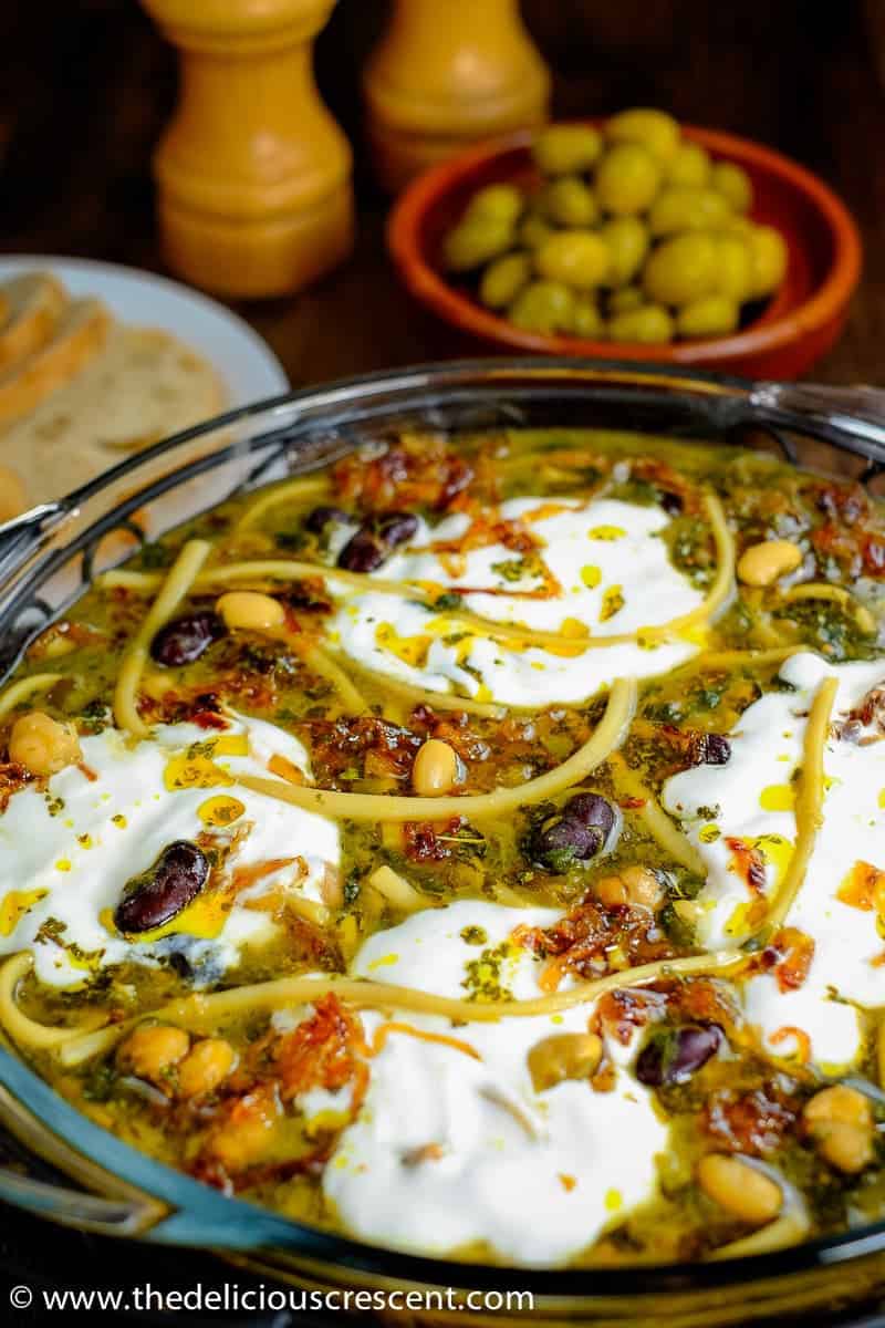 Ash reshteh served in a bowl with bread and olives.