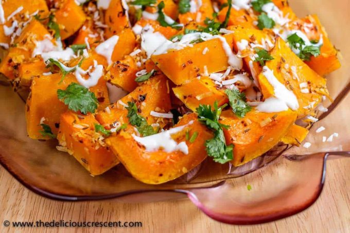 Spiced butternut squash topped with herbs and yogurt sauce in a glass plate.
