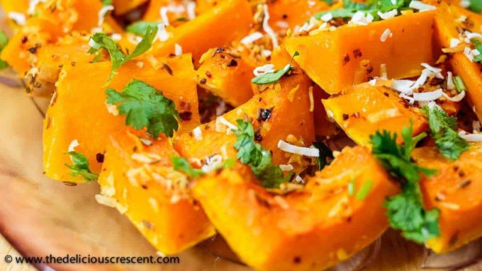 Slices of roasted butternut squash topped with red chili flakes, dried coconut and herbs.
