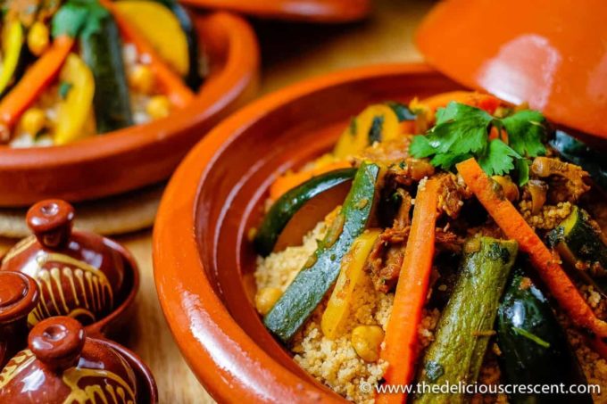 Lamb and vegetable tagine with couscous in a brown dish placed on a table.