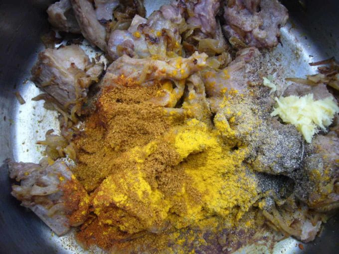Browned meat with spices and aromatics in a cooking pot.