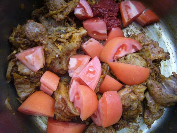 Tomatoes and tomato paste added to browned and spiced meat.