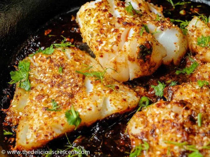 Close view of fish with tamarind sauce and herbs in a cast iron skillet.