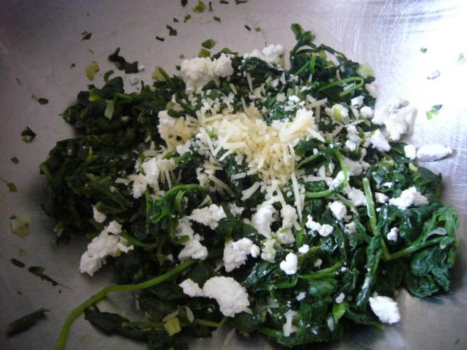Adding cheese to sauteed spinach to make spinach eggs.