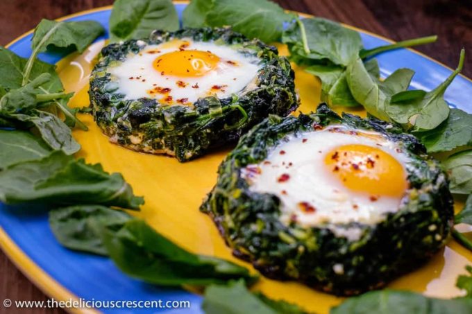 A front view of spinach egg stuffed mushrooms served on a plates with fresh spinach leaves.