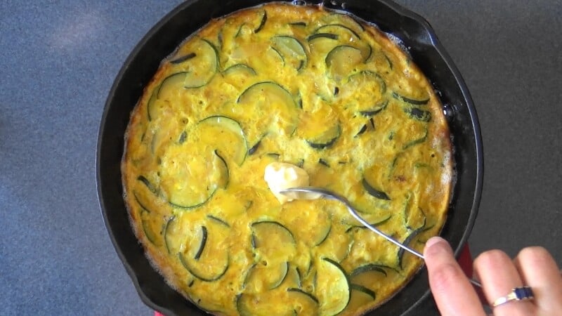 A pat of butter being spread on top of baked frittata.