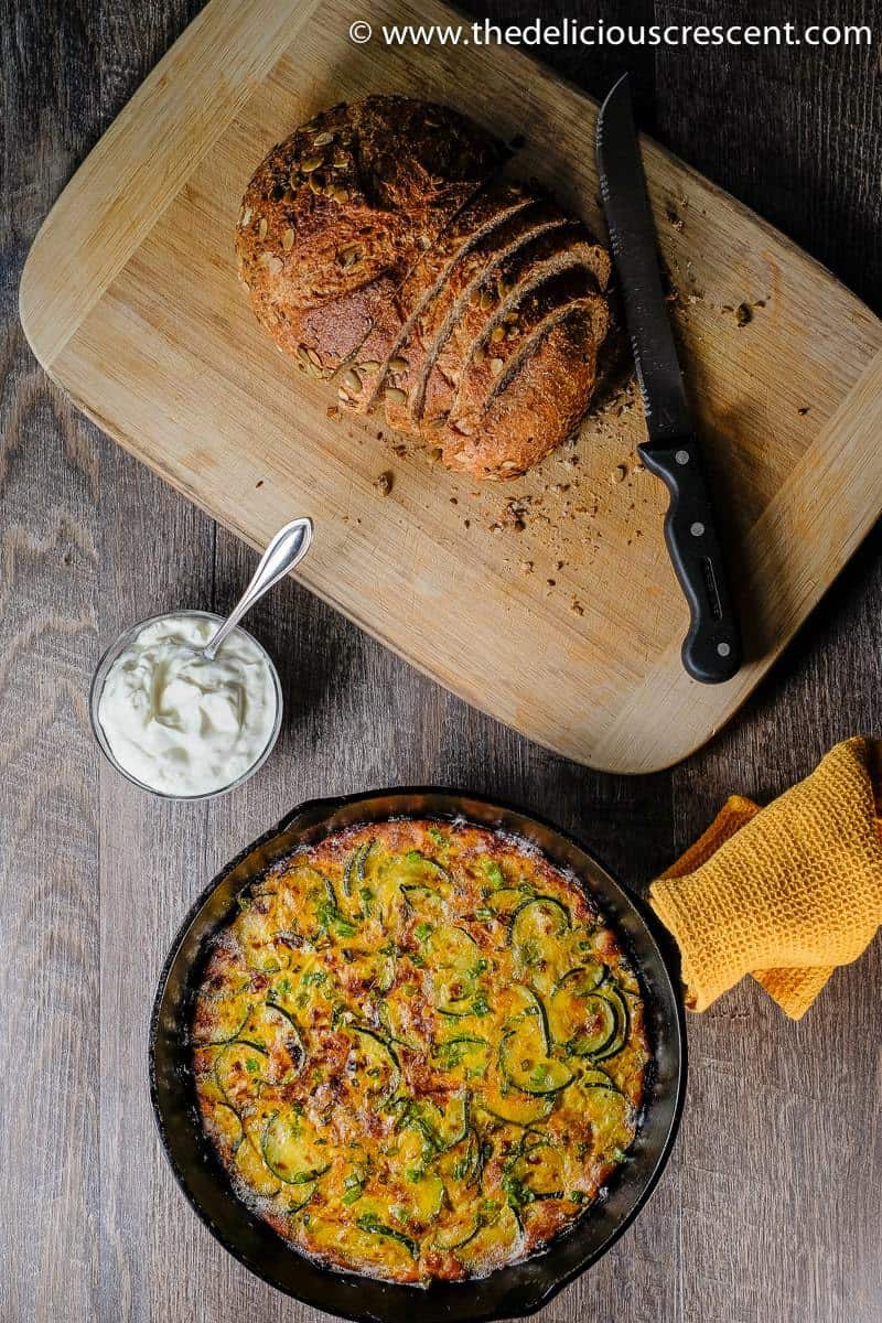 Overhead view of zucchini frittata served with sliced bread on a wooden board.