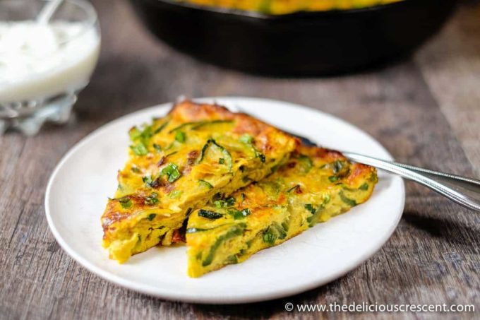 Two slices of Persian zucchini frittata served with a yogurt dip in a glass bowl.