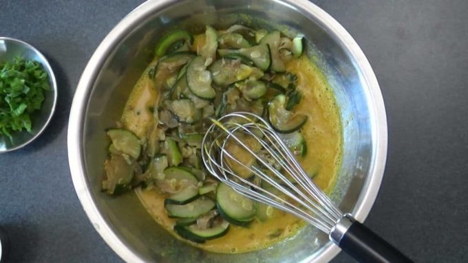 Sauteed zucchini and onions being mixed with eggs and spices to make Persian kuku.