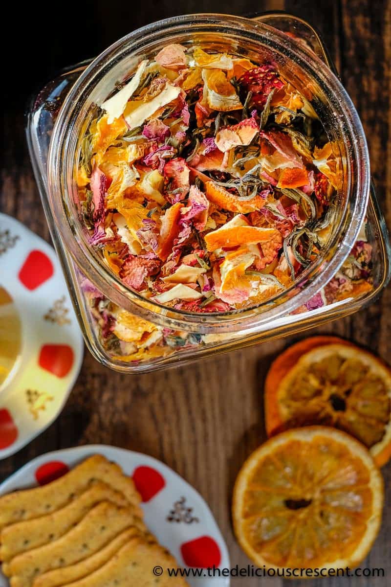 Homemade tea blend in a glass jar placed next to some crackers and dried orange slices.