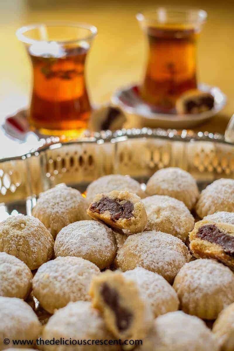 Maamoul are buttery date filled middle eastern cookies that will melt in your mouth and are utterly delicious. Naturally sweetened with dates these have minimal added sugar. They are popular at Eid, Christmas and other holidays. This recipe shows you how to make it with a mold or by hand. These vegetarian cookies are nut-free, egg-free and freezer friendly. #cookie #Mediterraneandietrecipe Maamoul - date filled cookies served with tea.
