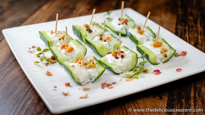 Small bite-sized cucumber boats filled with yogurt salad and decorated with toppings.