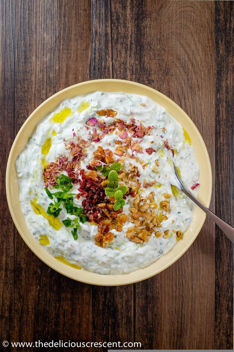 Mast-o khiar served in a bowl with toppings and placed on the table.