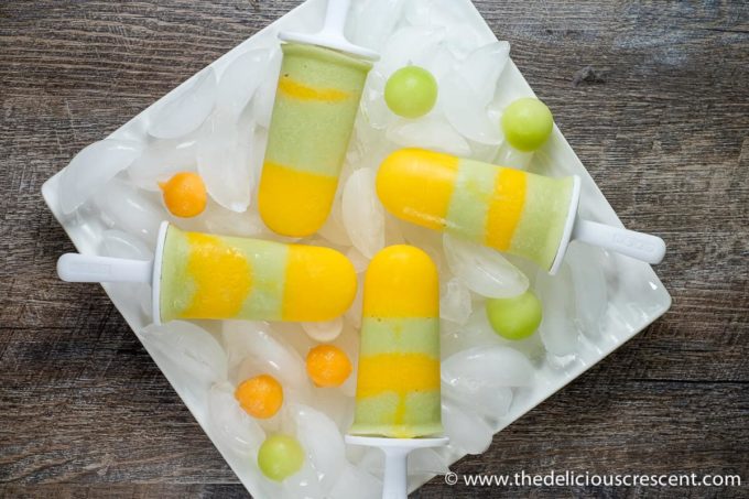 Four melon popsicles placed on a stack of ice in a plate.