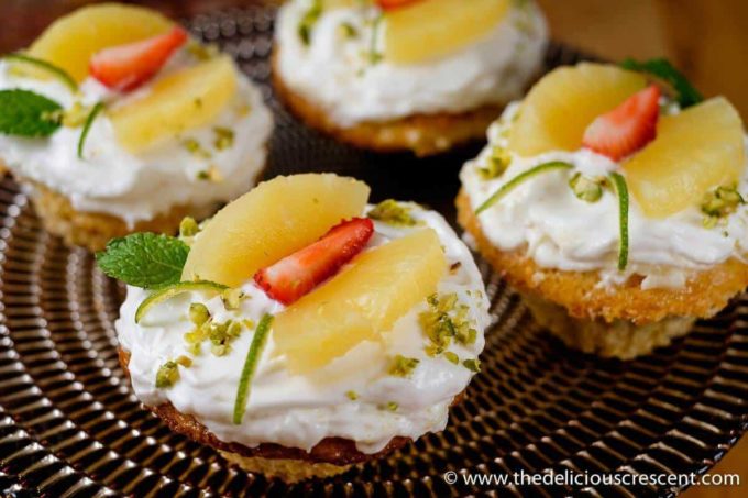 Cupcakes topped with icing and decorated with fruit and served on a plate.