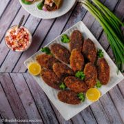 Fish cakes served on a plate with onions and lemon slices.