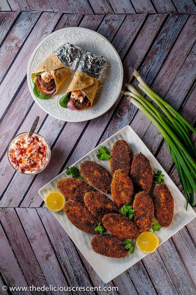 Indian fish cakes (fish shami kabab) crispy outside, soft in the center, these richly flavored spicy patties are a terrific appetizer. Easy, healthier, low carb and made with salmon. Freezes beautifully! Gluten free option. #salmon #appetizer #lowcarb #easyrecipe #freezercooking #fish #snacks Overhead view of spicy fish cakes served on the table with wraps.