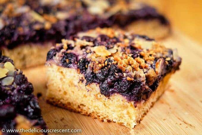 German Blueberry bread is the best breakfast bread ever. Sweet and juicy blueberries with a streusel topping and toasted almonds on a soft cake like yeast bread. Two recipes - classic and healthier. Healthy version with less sugar, less saturated fat, extra fiber and more goodness. This German blueberry cake with crumb topping is good for dessert too and is freezer friendly. #healthybreakfast #blueberries Close up view of a German blueberry bread piece.